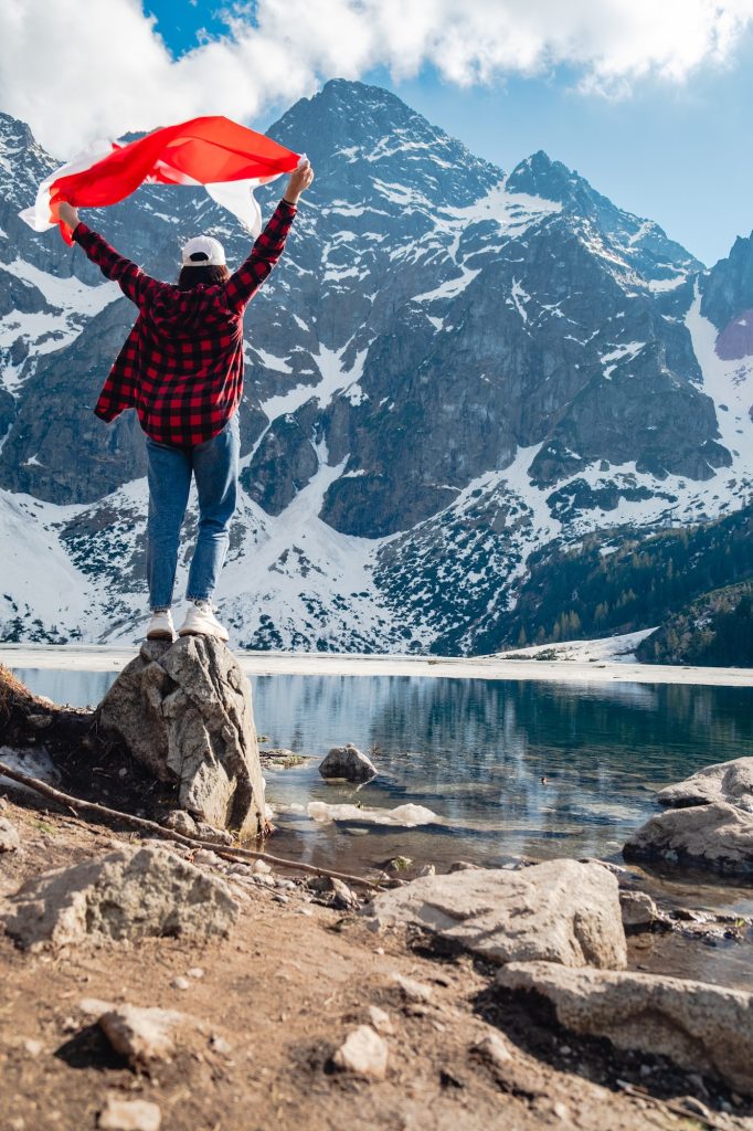 A woman with Poland flag is standing on the shore of a lake. Morskie Oko